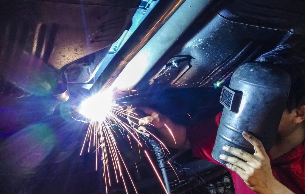 Lasser voert nauwkeurig tig lassen uit aan de onderkant van een voertuig in een werkplaats