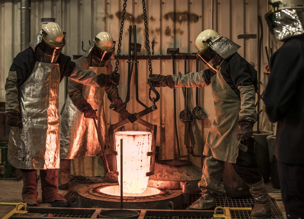Medewerkers in beschermende kleding en helmen voeren thermisch verzinken uit bij het gieten van gesmolten metaal in een industriële smeltoven