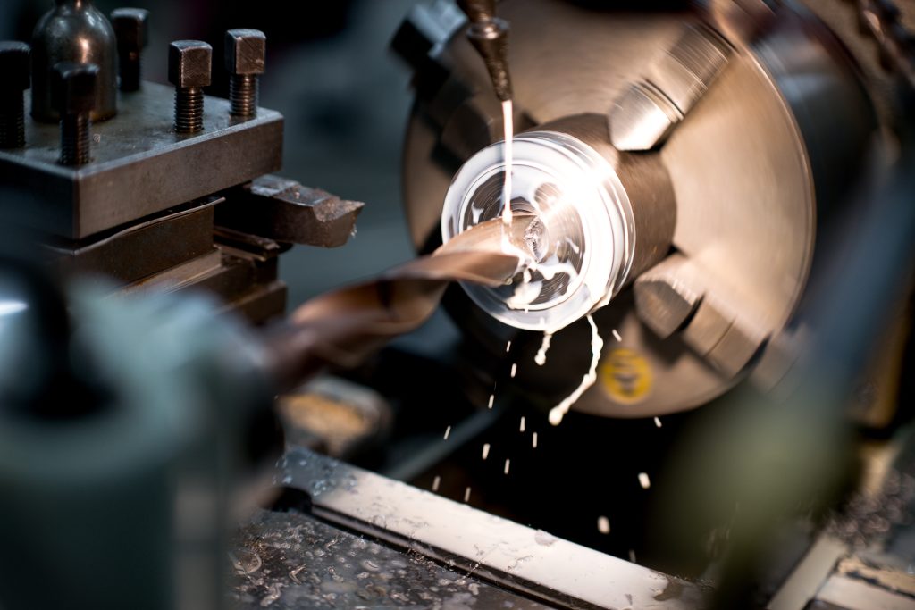 Close-up van fijnmechanisch draaiwerk op een draaibank waarbij een metalen onderdeel met precisie wordt geboord en gekoeld.