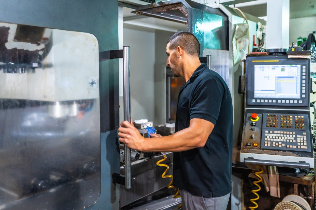 Technicus bedient het controlepaneel van een moderne machine voor nauwkeurig cnc freeswerk in een metaalwerkplaats